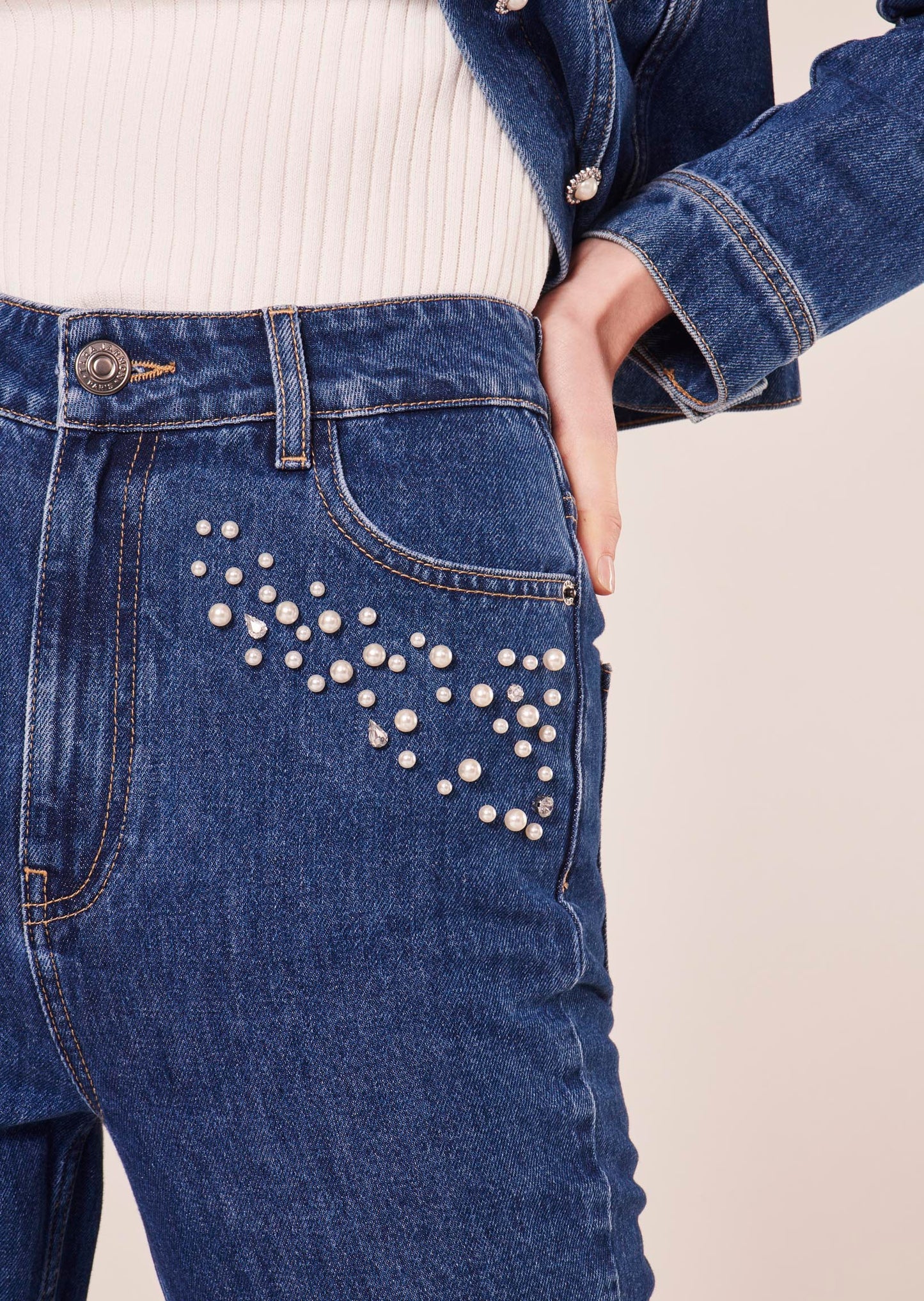 Blue denim jeans featuring a straight cut, zip closure, and 5 pockets with embroidered pearls, and rhinestones at the front.