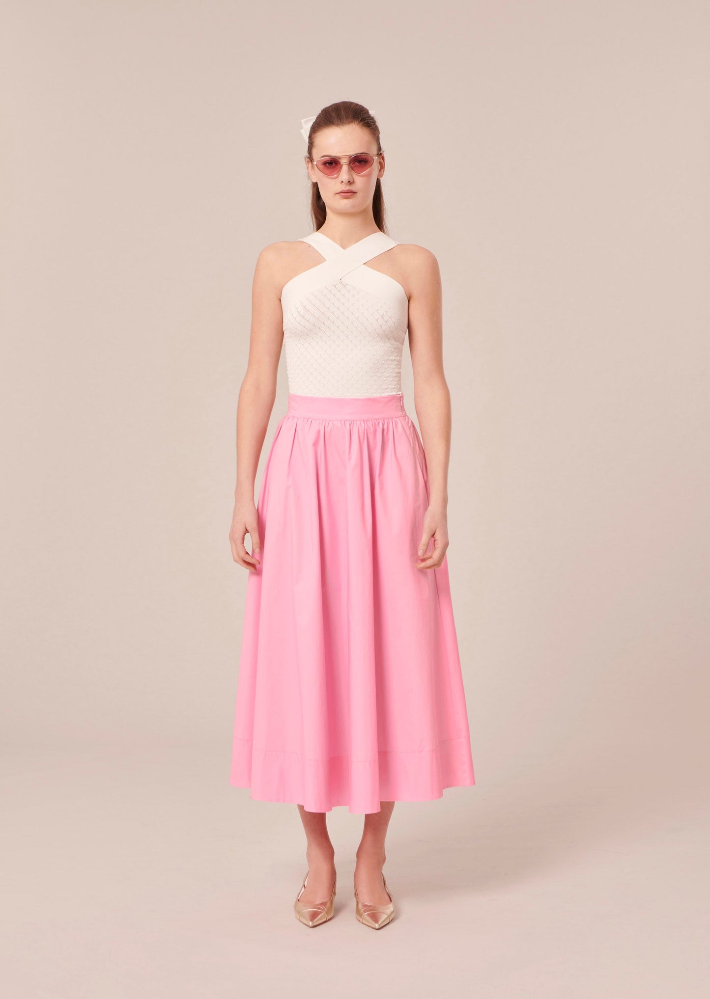 Model wearing Tara Jarmon white crop top that crosses at the front and back with long pink skirt.