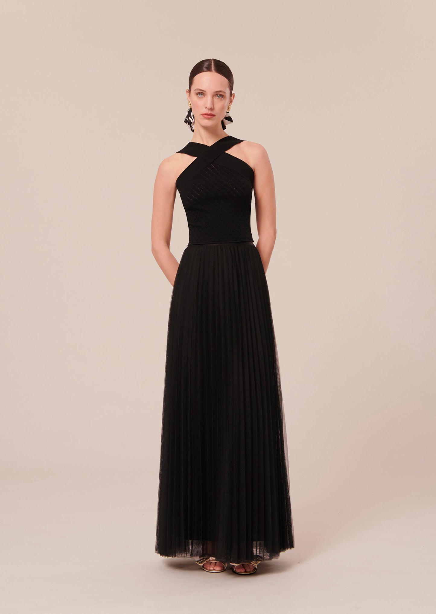 Model wearing Tara Jarmon black crop top that crosses at the front and back with long pleated black skirt.