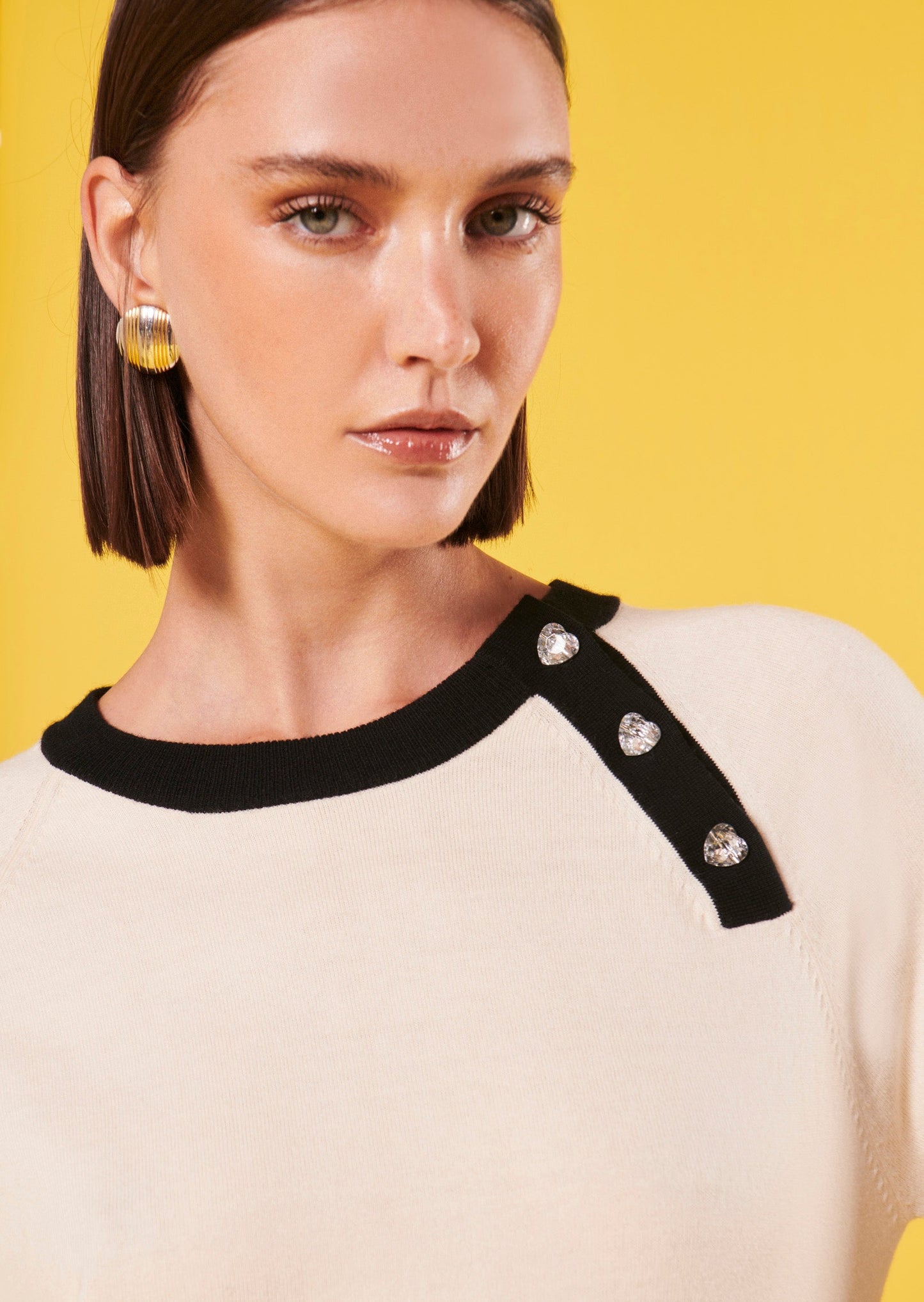 Ecru sweater with heart-shaped jeweled buttons decorating its left shoulder.