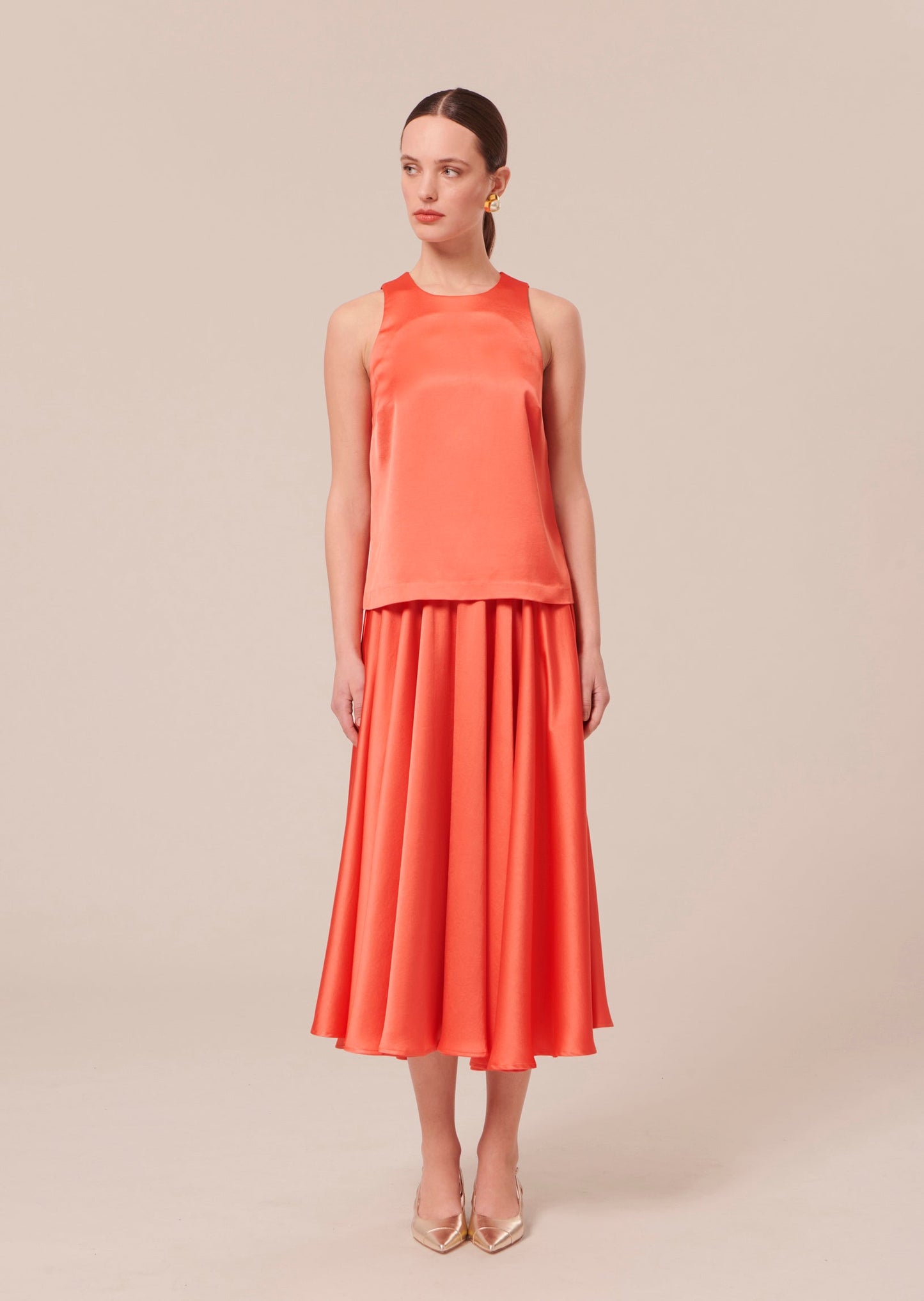 Model wearing Tara Jarmon Flowing Satin Top in Coral with Round Neckline.