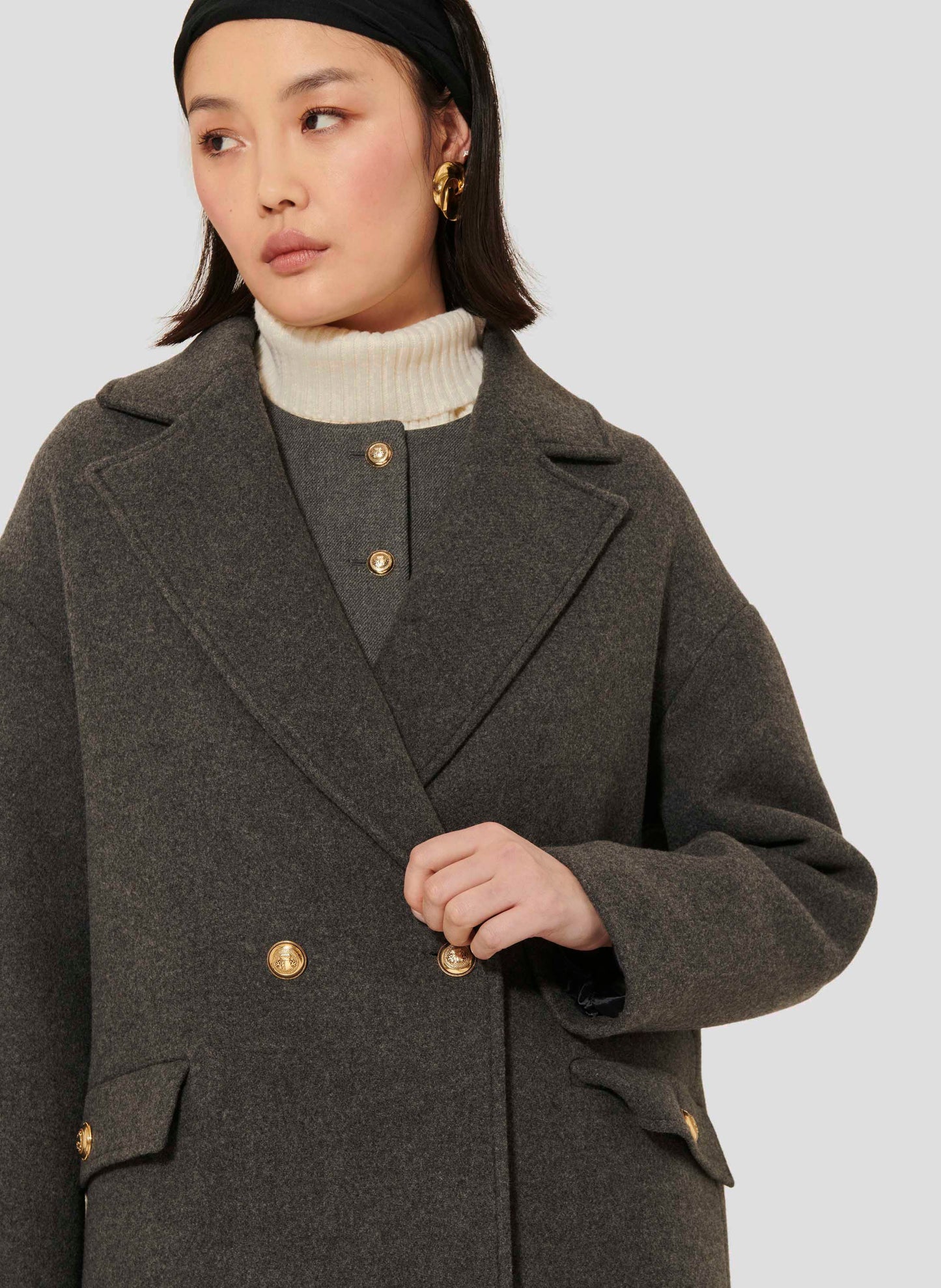 Long gray sheepskin coat with flap pockets and gold buttons.