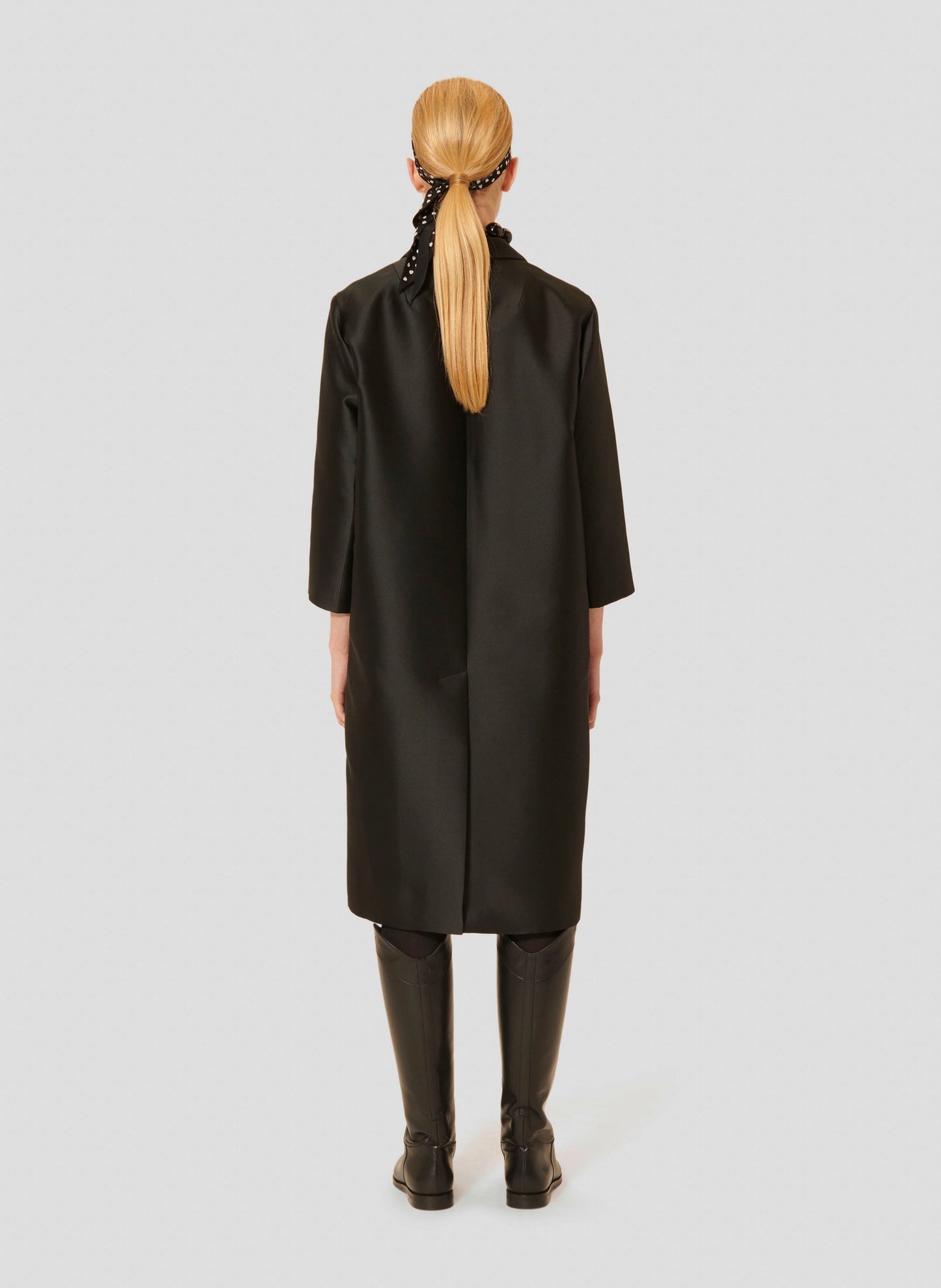 Long black duchesse satin coat with a wide, straight cut, lapel collar, 3/4-length sleeves and two large patch pockets on the sides.