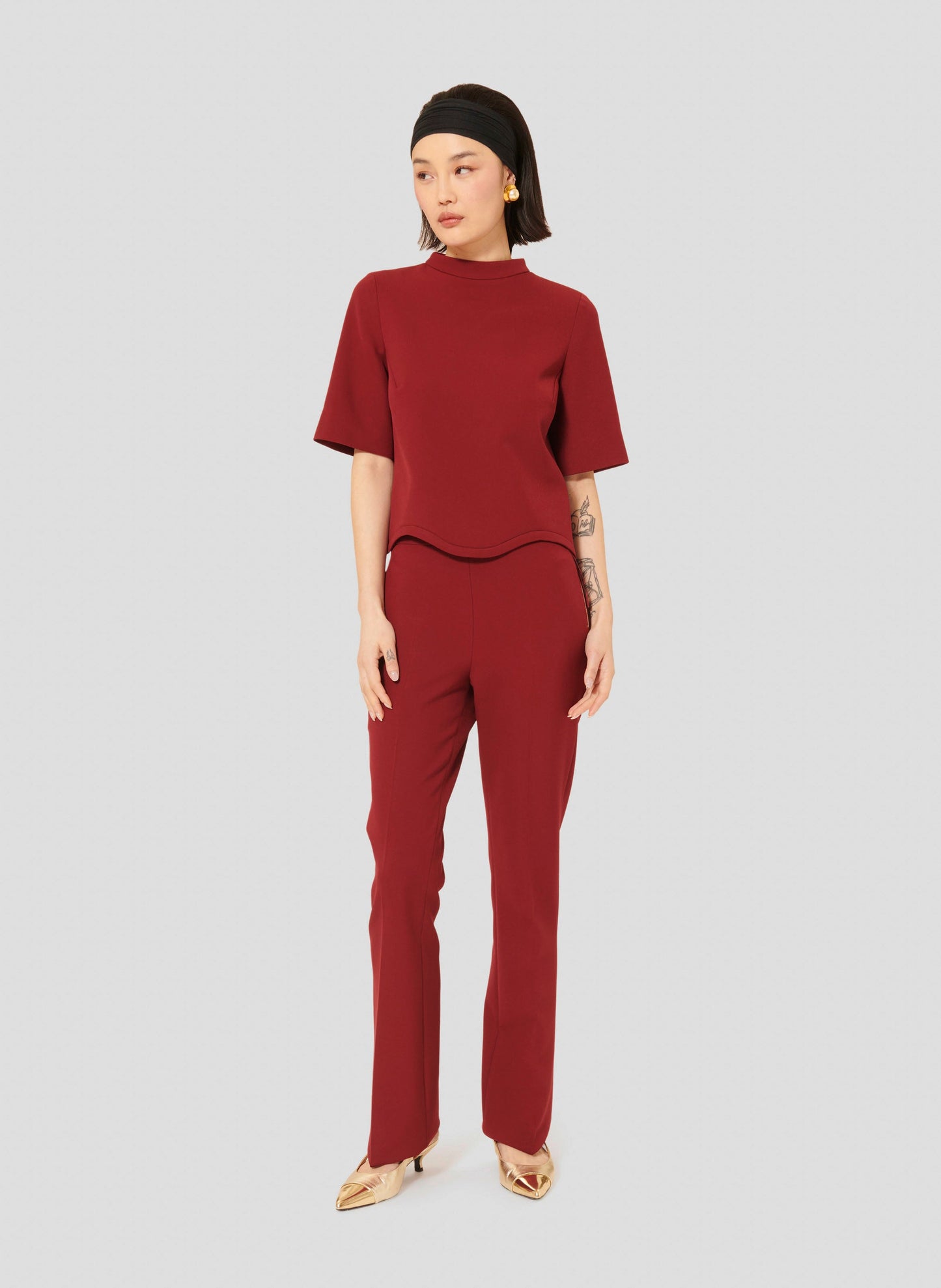 Model wearing Tara Jarmon Burgundy Stretch Pants with Mid-Rise Waist, Side Zip and Matching Short Sleeves Burgundy Top.