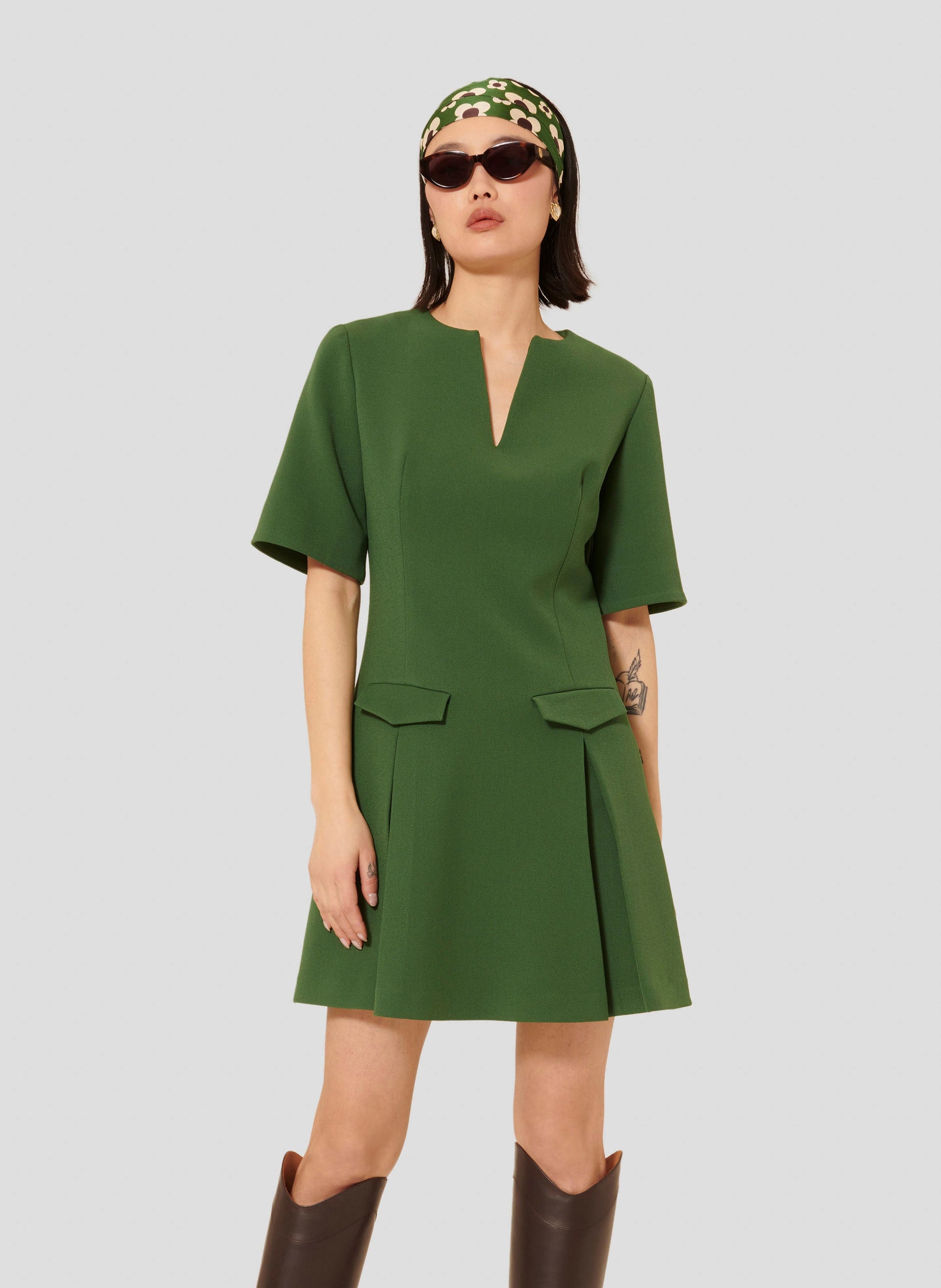 Model wearing Tara Jarmon Green Crepe Short Dress with Pleated Skirt and Flap Pockets.